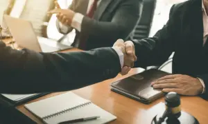 Uścisk dłoni prawników przy stole z notatnikiem i młotkiem sędziowskim. Verba volant, scripta manent – słowa mijają, pisma zostają.