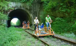Rodzina na drezynach w Bieszczadach pokonuje malowniczy tunel kolejowy, ciesząc się zielenią i aktywnym wypoczynkiem.