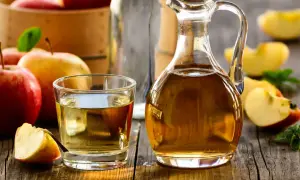 Aceto di mele in caraffa e bicchiere, con mele fresche. Un rimedio naturale per un bucato morbido.