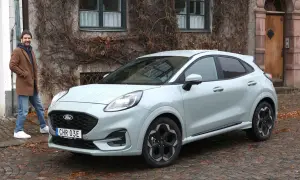 Man står bredvid Fords minsta modell, en ljusgrå Puma, framför ett gammalt hus med murgröna.