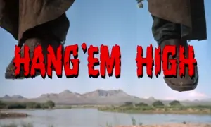 Nogi w kowbojkach wiszą nad rzeką. Czerwony napis "HANG 'EM HIGH" sugeruje westernowe porachunki.