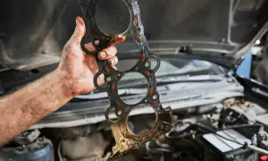 Brudna uszczelka pod głowicą, dowód na konieczność naprawy. Mechanik trzyma ją w ręku, gotowy do wymiany.