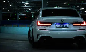 Vue arrière d'une BMW blanche dans un parking sombre. L'éclairage de la plaque d'immatriculation est bien visible, soulignant son caractère obligatoire.