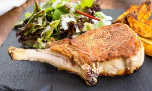 Saftiges Kotelett im Backofen, goldbraun gebraten, serviert mit knusprigen Kartoffelspalten und frischem Salat.