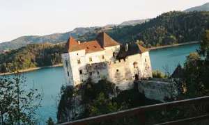 Zamek w Niedzicy, majestatycznie wznoszący się nad turkusową wodą, otoczony zielonymi wzgórzami.