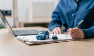 Osoba podpisuje dokumenty dotyczące wyrejestrowania pojazdu online. Obok leży model samochodu i kluczyki.