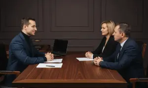 Trzy osoby przy drewnianym stole, laptop, dokumenty. Prawnik przedstawia potwierdzenie za zgodność z oryginałem.