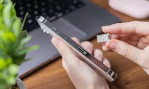 Ręka trzyma duplikat karty SIM obok telefonu.