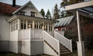 Vitt hus med glasveranda, stjärnor i fönstren och en röd stuga i bakgrunden. Glasveranda inspiration för ett mysigt hem.