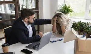 Mężczyzna pociesza kobietę przy biurku, na którym leży laptop i dokumenty.