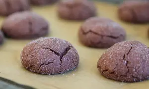 Mörka, sprickiga nutella kakor täckta med socker ligger på ett bakplåtspapper.