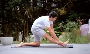 Un homme s'étire sur un tapis, se demandant combien de temps durent les courbatures après son entraînement.