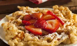 Strauben croccanti, guarniti con fragole fresche e zucchero a velo. Una deliziosa ricetta per un dolce da fiera.