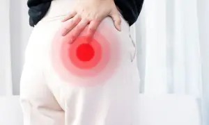 Person håller handen mot höften där en röd cirkel indikerar smärta, möjligen relaterad till piriformis triggerpunkt.