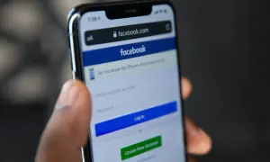 Dłoń trzyma smartfon z ekranem logowania Facebooka. Szukasz sposobu, jak odzyskać konto na FB bez maila i telefonu?