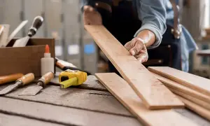 Carpintero examinando tablas de madera, listo para aprender como quitar pintura de la madera. Herramientas de carpintería a la vista.