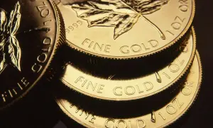 Stos złotych monet z liściem klonu i napisem "FINE GOLD".