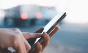 Dłoń dotyka ekranu smartfona, szukając informacji, jak przywrócić ustawienia fabryczne w telefonie. W tle rozmyte światła.