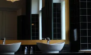 Elegante bagno nero design con due lavabi bianchi, rubinetteria cromata e specchio dorato. Pareti rivestite di piastrelle nere lucide.