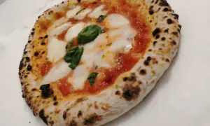 Une authentique pizza napolitaine, avec sa croûte gonflée et légèrement brûlée, garnie de sauce tomate, de mozzarella fondante et de feuilles de basilic frais.