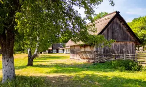 Skansen w Klukach: drewniane chaty z krytymi strzechą dachami, otoczone zielenią i sielskim krajobrazem.
