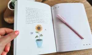 Een open dagboek met een zonnebloem en vlinder illustratie. Een roze pen ligt op de rechterpagina, klaar om gedachten uit je hoofd op te schrijven.
