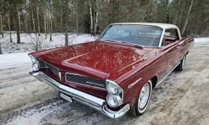 Röd Pontiac 60-tal, en klassisk bil med kromdetaljer, står parkerad i snöig skogsmiljö.