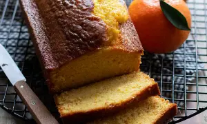 Plumcake all'arancia appena sfornato, dorato e profumato, con fette morbide e arance fresche accanto.