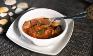 Polipetti in purgatorio, un piatto di mare con pomodorini e pane tostato, servito in una ciotola bianca su un tavolo scuro.
