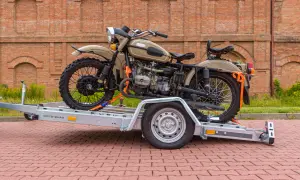 Solidne mocowanie motocykla do transportu na przyczepie. Pomarańczowe pasy zabezpieczają pojazd przed przesuwaniem.
