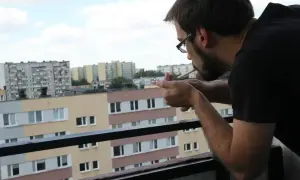 Mężczyzna zapala papierosa na balkonie, patrząc na blokowisko. Czy można palić na balkonie? To pytanie zadaje sobie wielu mieszkańców.