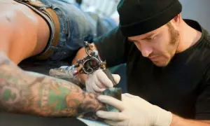 Artista de tatuajes concentrado, considerado el mejor del mundo, trabajando en un brazo con diseño detallado.