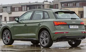 Zielony Audi Q5 Sportback na mokrym parkingu, z budynkami w tle.