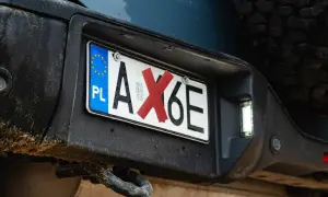 Polski numer rejestracyjny pojazdu AX6E z czerwoną naklejką na literze X.