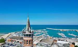 Torre con antenne domina il porto civitanova, pieno di barche e con il mare azzurro sullo sfondo.