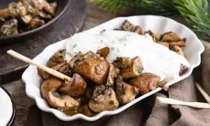 Gebratene Champignons mit Kräuterquark, wie vom Weihnachtsmarkt, auf einem weißen Teller mit Holzspießen.