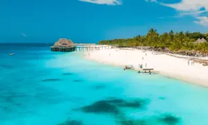 Rajskie zanzibar wakacje: biała plaża, palmy, turkusowa woda i drewniany pomost z domkami na wodzie. Idealne miejsce na relaks.