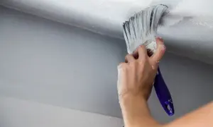 En hand målar om taket med en vit färg. Det är ett hemmaprojekt för att fräscha upp rummet.