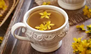 Aromaticzna herbata z dziurawca w ozdobnej filiżance, pływające żółte kwiaty dodają uroku.