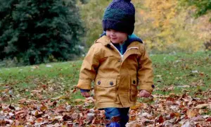 Mały chłopiec w jesiennej kurtce i czapce spaceruje po parku wśród opadłych liści. Idealne miejsce, gdzie na weekend z dzieckiem jesienią.