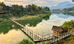 Mosty bambusowe nad rzeką, chatka z trawy, bujna zieleń i góry w oddali. To idealne miejsca, by zobaczyć **laos co zobaczyc**.