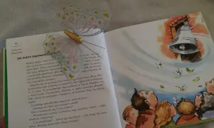 Otwarta książka z ilustracją dzwonu i dzieci patrzących w górę. Motylowa zakładka ozdabia stronę z tekstem o tym, jak ludzie zapomnieli o Bogu.