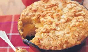 Ein goldbrauner Reisauflauf mit Apfelstücken, bedeckt mit knusprigen Mandelblättchen. Ein Löffel hebt ein Stück heraus.