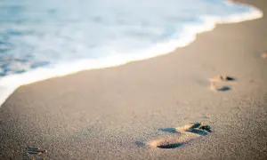 Ślady stóp na piaszczystej plaży, gdzie fale obmywają brzeg. Choć w Polsce jest tylko jedno morze, Bałtyk, to jego piękno jest niezmierzalne.