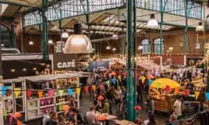 Buntes Treiben auf einem Street Food Festival in Berlin. Menschen schlendern zwischen Ständen mit Leckereien unter einer beeindruckenden Glasdachkonstruktion.