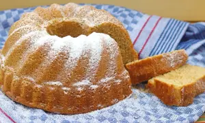 Puszysta babka z owocami, oprószona cukrem pudrem, czeka na spróbowanie. Obok leżą dwa kawałki ciasta.