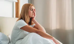A young woman woke up with a headache, grimacing and holding her forehead as she sits in bed.