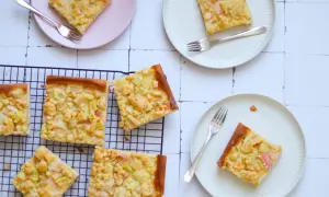 Saftiger Rhabarberkuchen auf Hefeteig mit Streuseln, auf Tellern und einem Kuchengitter arrangiert.