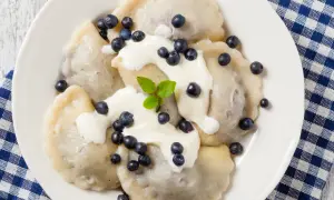 Pyszne pierogi z jagodami, polane śmietaną i posypane świeżymi owocami. Idealne na letni deser.