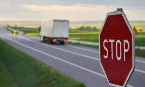 Czerwony znak stop na poboczu drogi, przed którym jedzie ciężarówka.